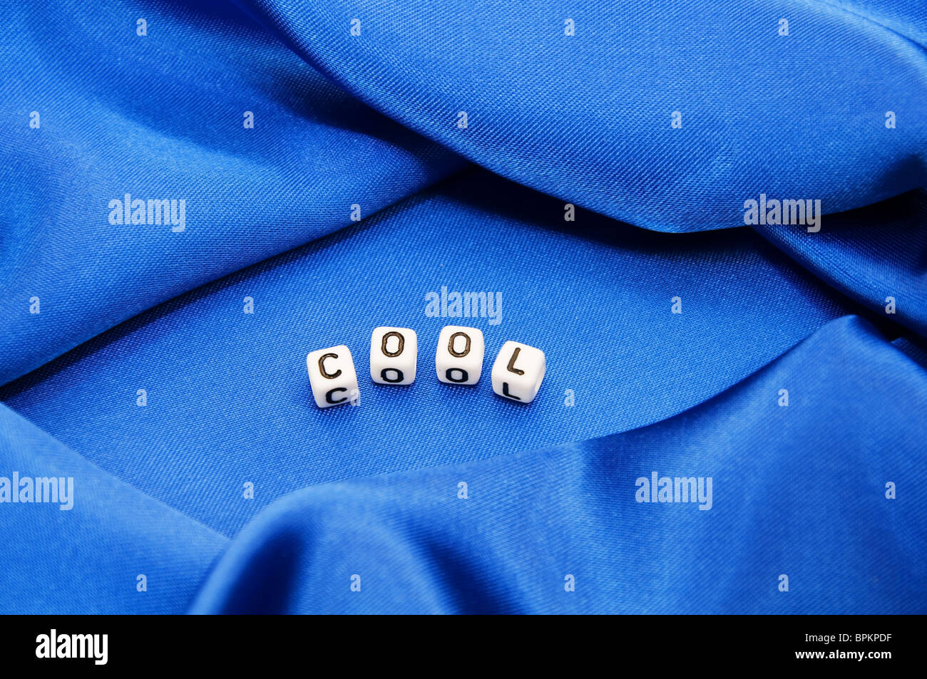 Royal blue satin background with rich folds and wrinkles for texture is the word cool in black and white cube lettering series Stock Photo