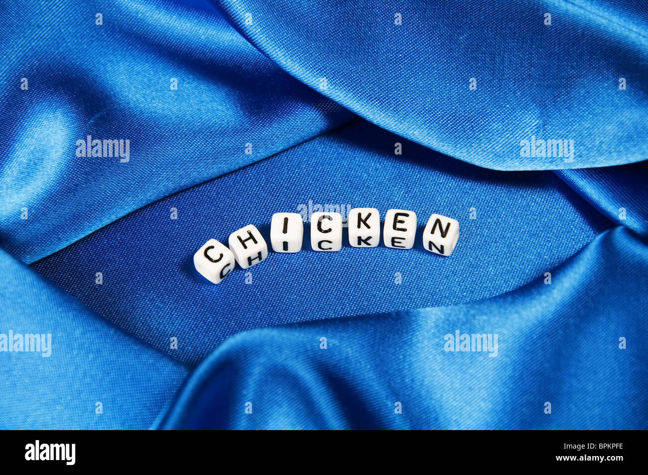 Royal blue satin background with rich folds and wrinkles for texture is the word chicken in black and white cube lettering serie Stock Photo