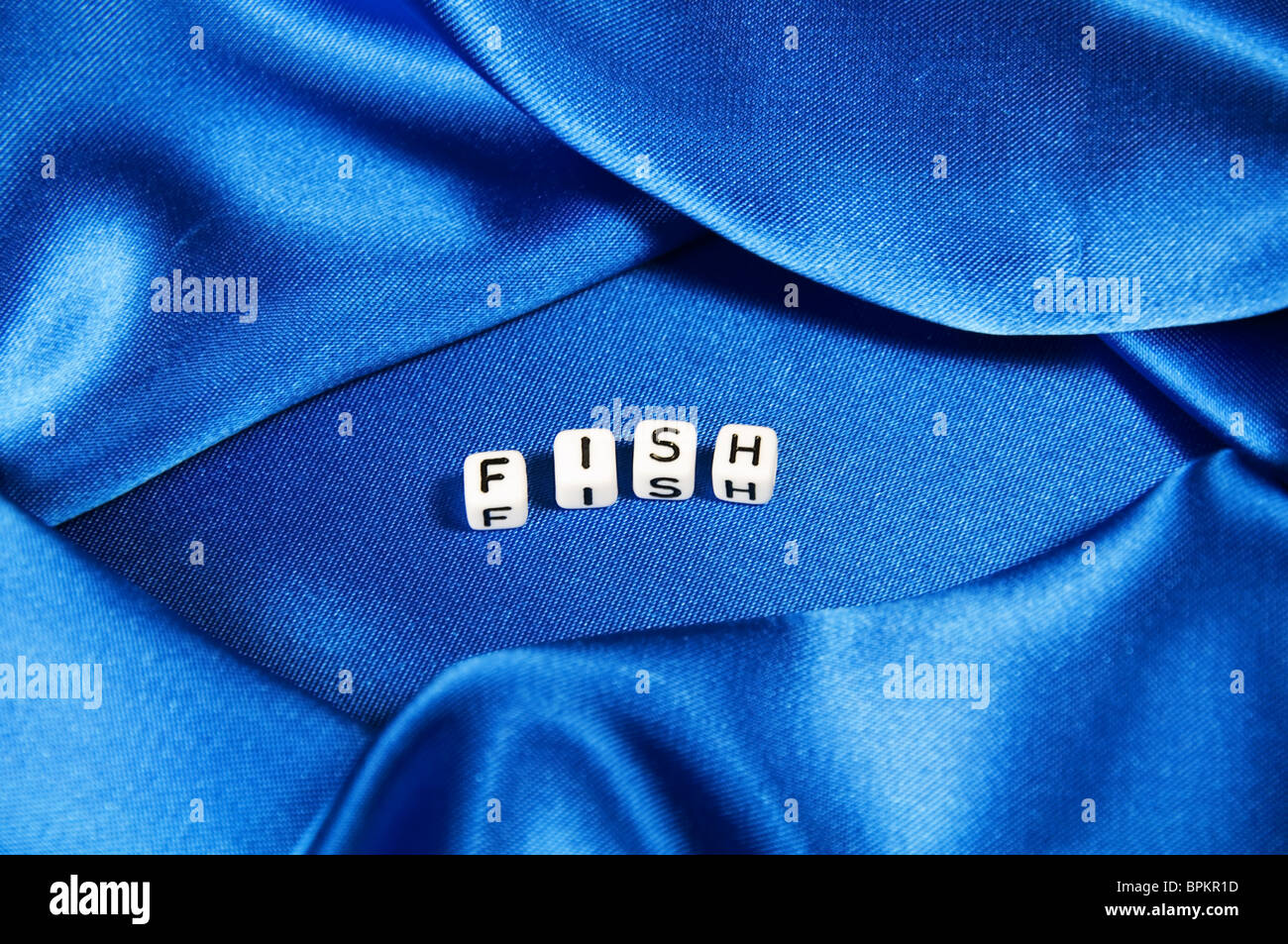 Royal blue satin background with rich folds and wrinkles for texture is the word fish in black and white cube lettering series Stock Photo