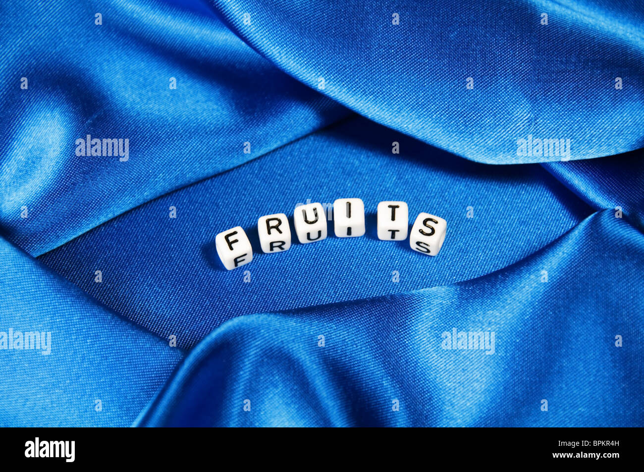 Royal blue satin background with rich folds and wrinkles for texture is the word fruits in black and white cube lettering series Stock Photo