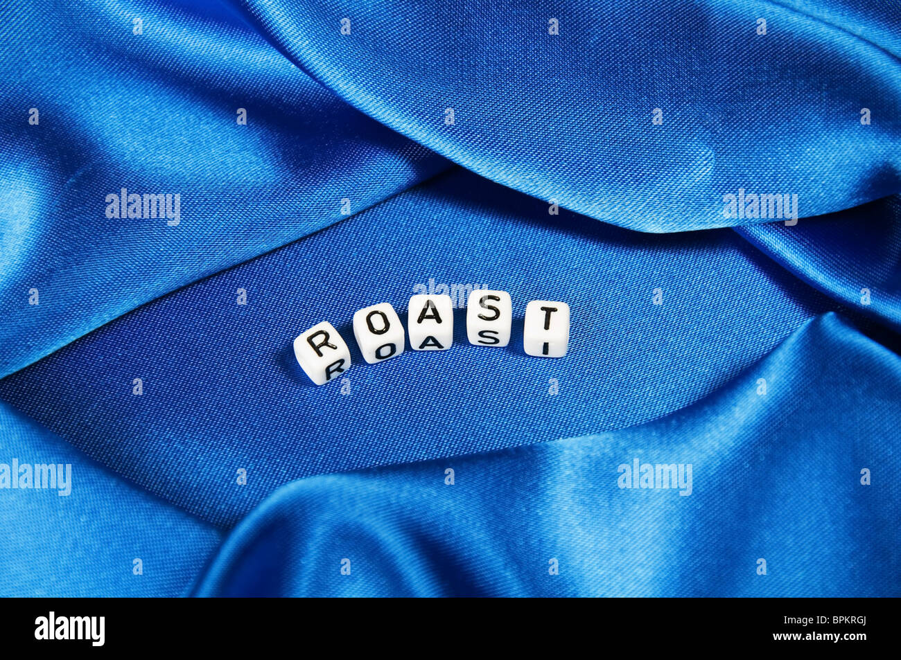 Royal blue satin background with rich folds and wrinkles  is the word roast in black and white cube lettering in this series Stock Photo