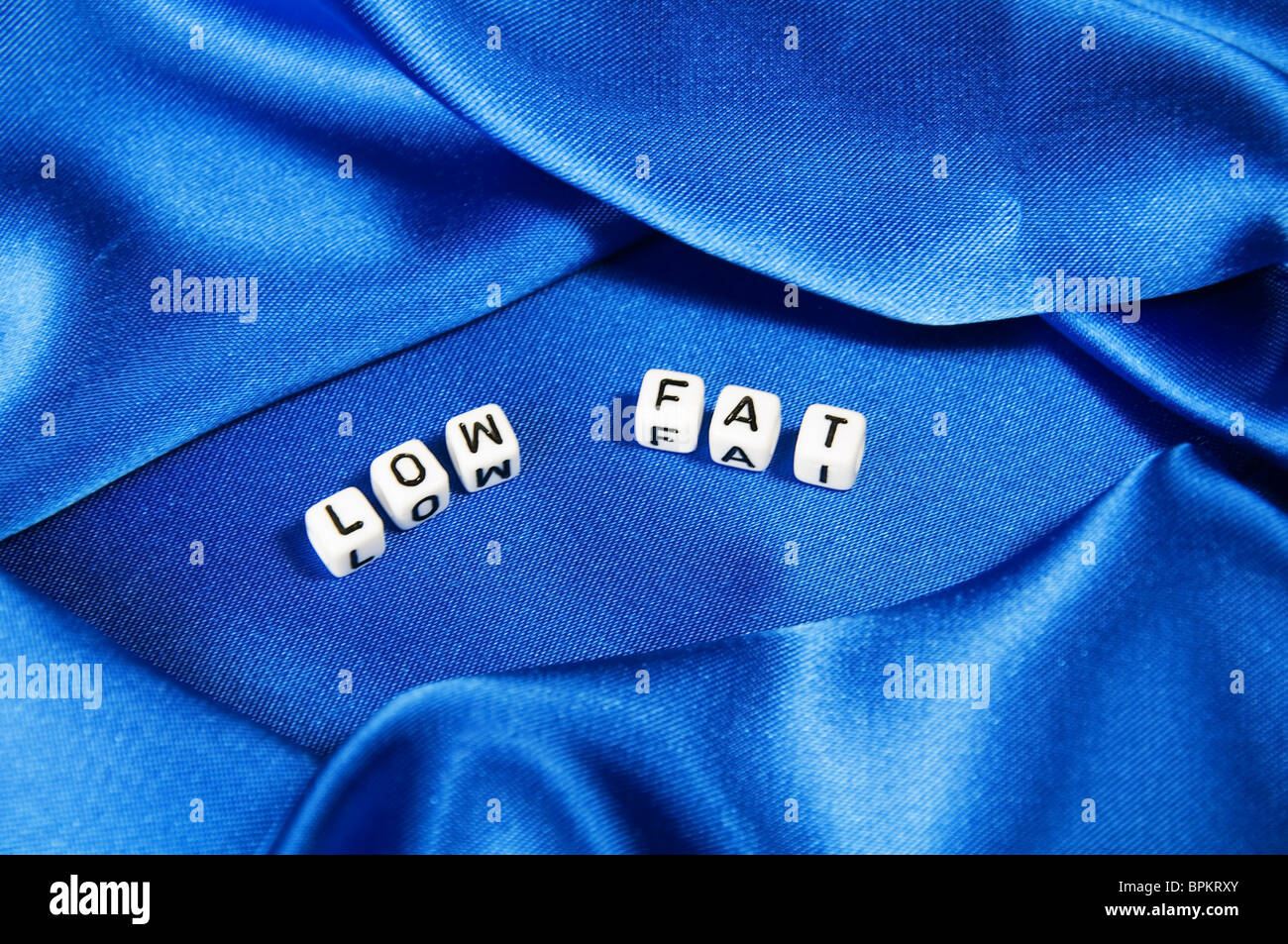 Royal blue satin background with rich folds and wrinkles for texture is the word low fat in black and white cube lettering serie Stock Photo
