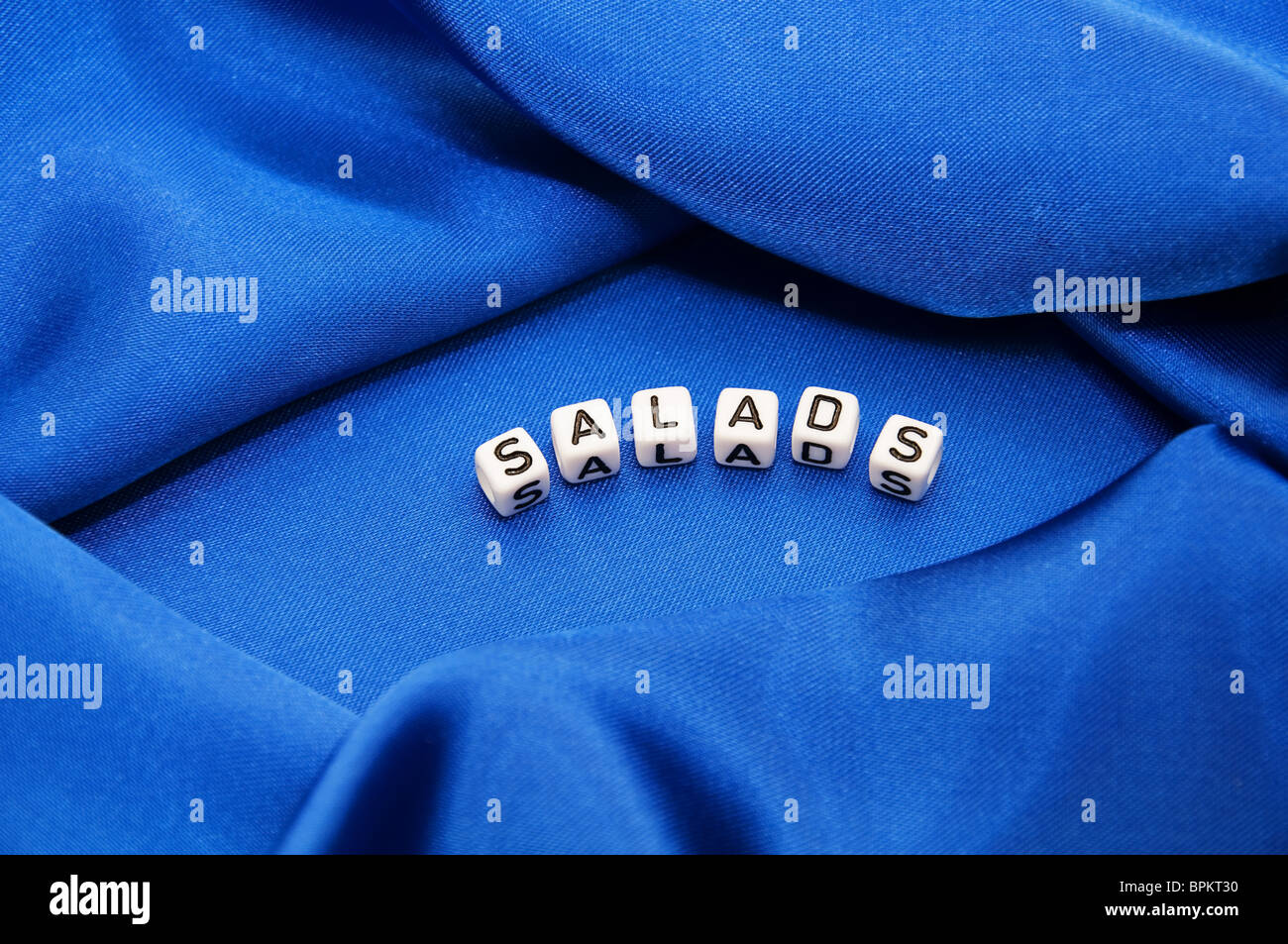 Royal blue satin background with rich folds and wrinkles for texture is the word salads in black and white  lettering series Stock Photo