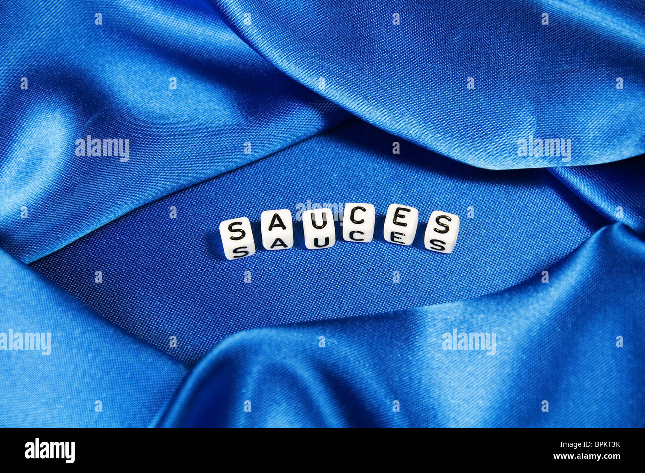 Royal blue satin background with rich folds and wrinkles for texture is the word sauces in cube lettering in this series. Stock Photo