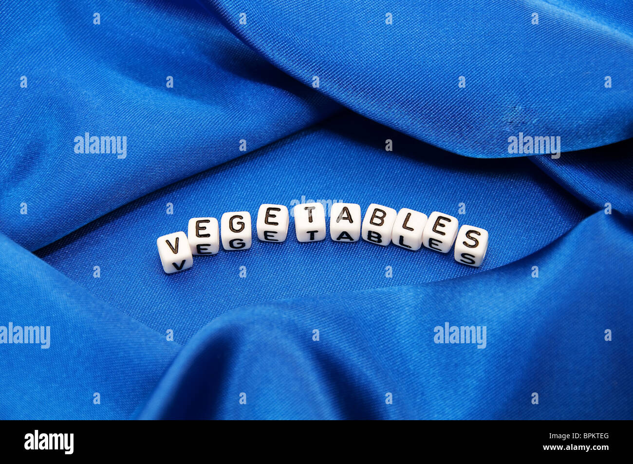 Royal blue satin background with rich folds and wrinkles for texture is the word vegetables in cube lettering series Stock Photo