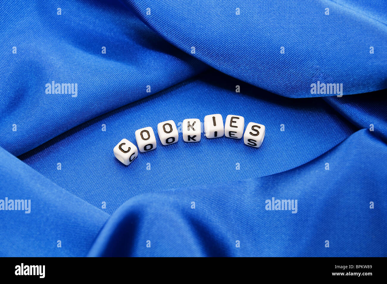 Royal blue satin background with rich folds and wrinkles for texture is the word cookies in black and white cube lettering serie Stock Photo