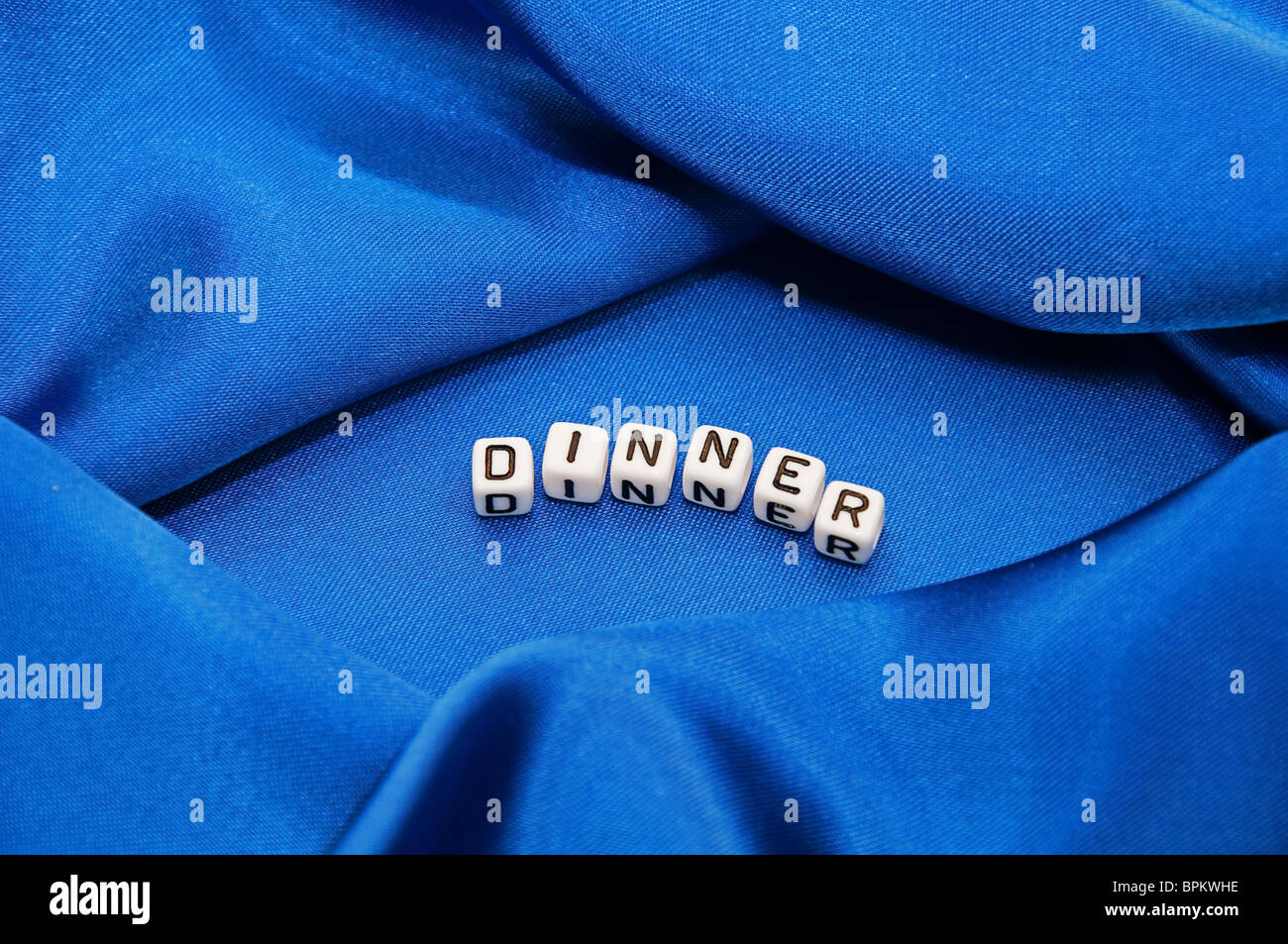Royal blue satin background with rich folds and wrinkles for texture is the word dinner in black and white cube lettering series Stock Photo