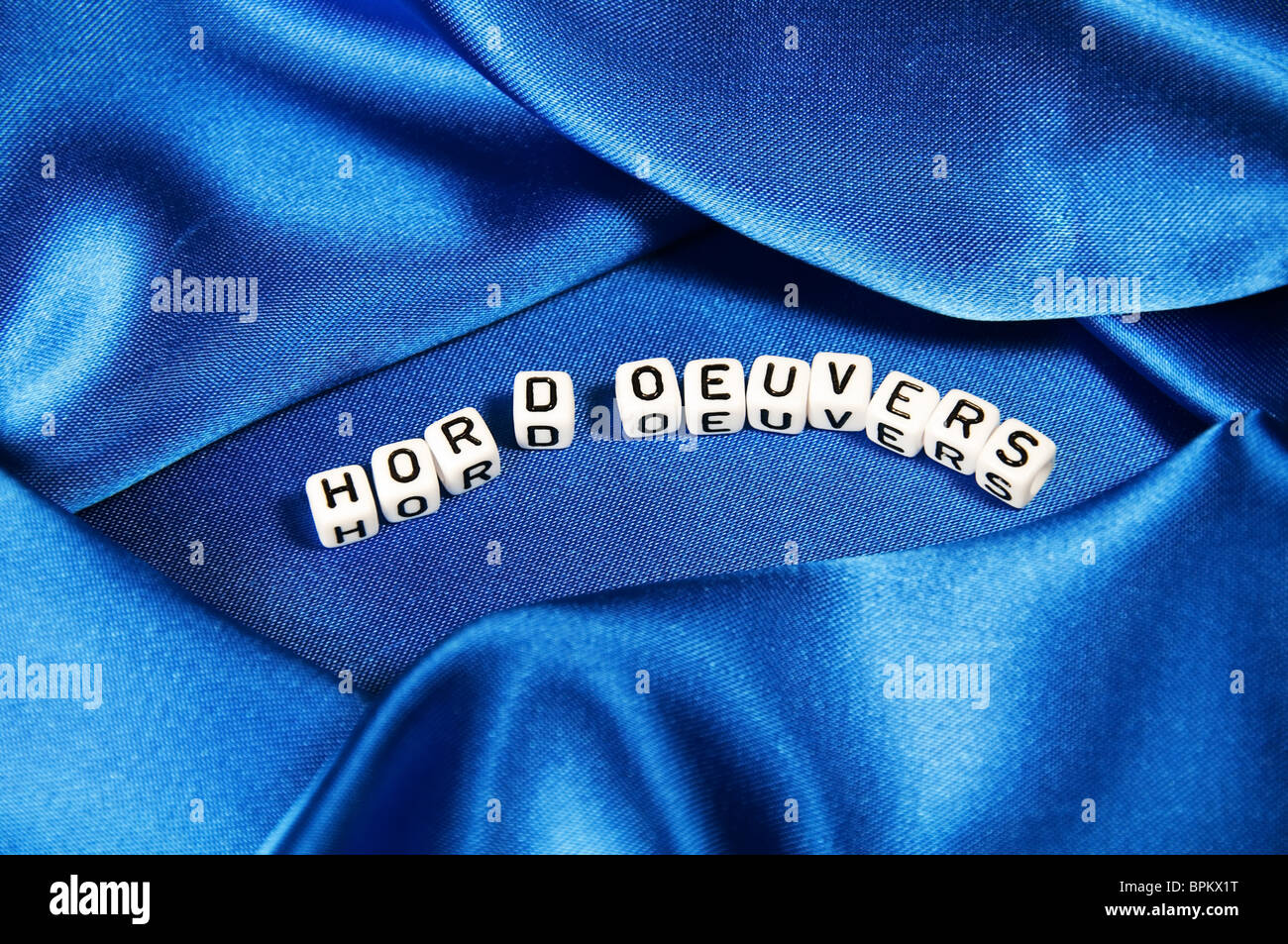Royal blue satin background with rich folds and wrinkles for texture is the word hor d'oeuvers in black and white cube lettering Stock Photo