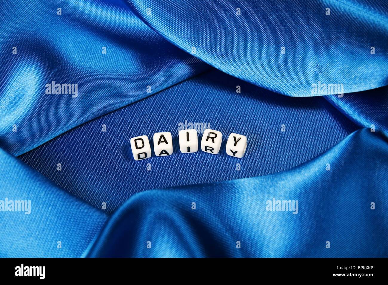 Royal blue satin background with rich folds and wrinkles for texture is the word dairy in black and white cube lettering series Stock Photo