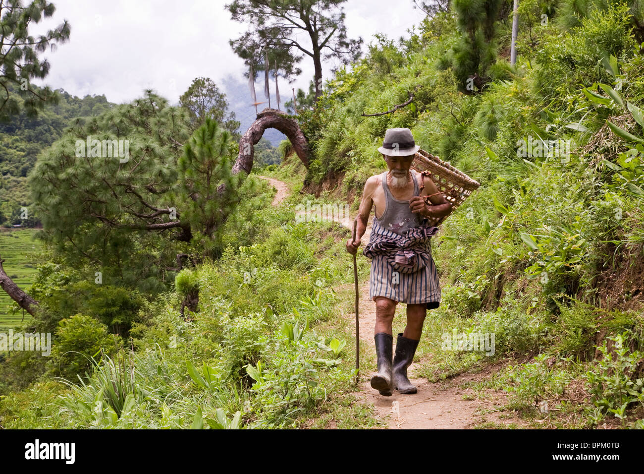Old Man with basket and staff on trail in Punakha Valley Bhutan Asia Stock Photo