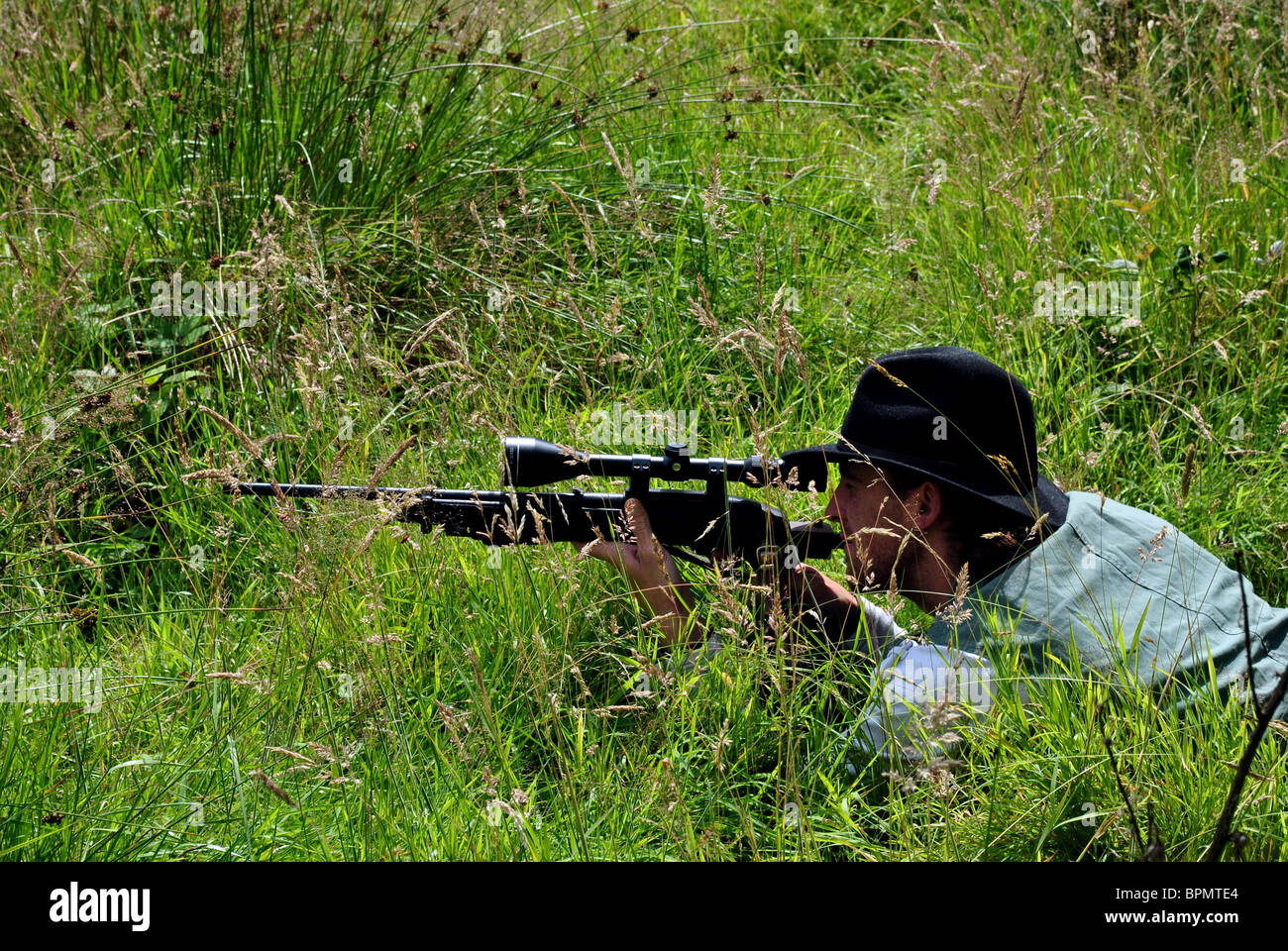 man lying in a meadow taking aim with a rifle Stock Photo