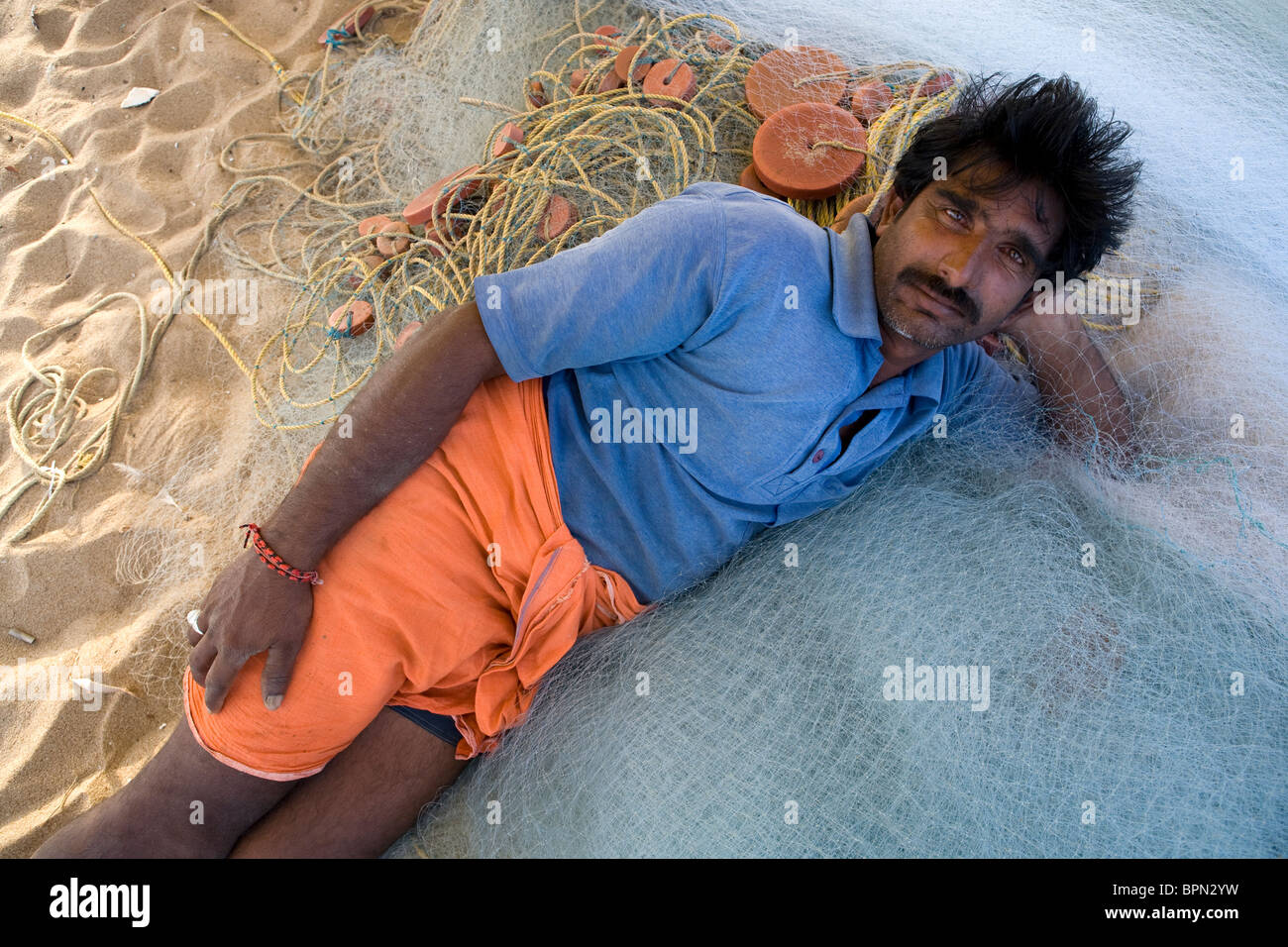 Indian fisherman is resting during his work of preparing fishing nets on the beach at the fishing village in Puri. Stock Photo