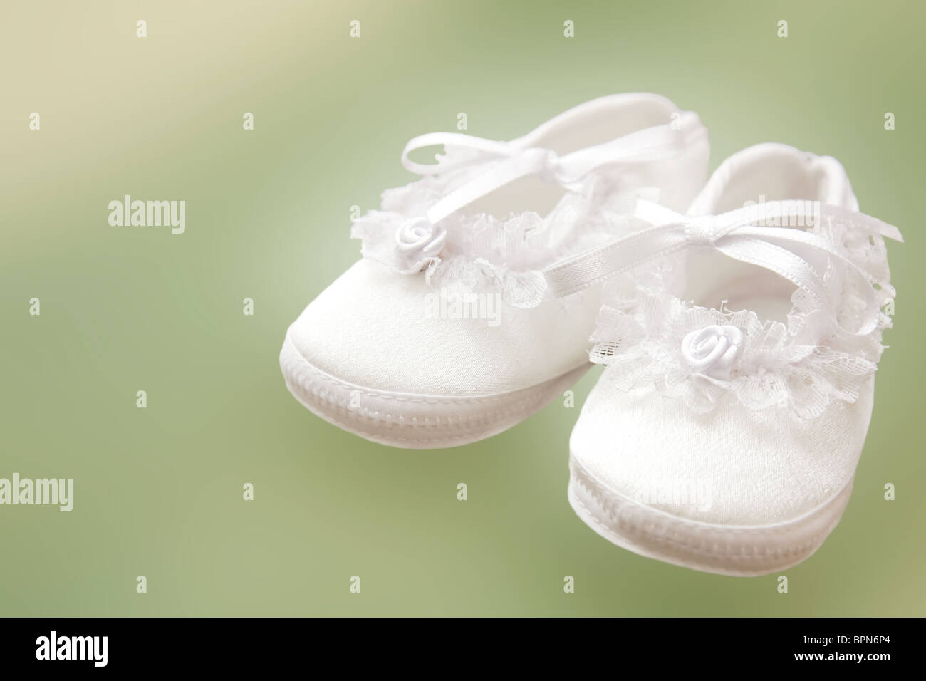 White baby shoes for christening on green background. Stock Photo