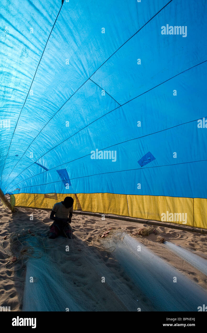 Young Indian fisherman is preparing fishing nets under a big blue tent in the late afternoon on the beach at the fishing village Stock Photo