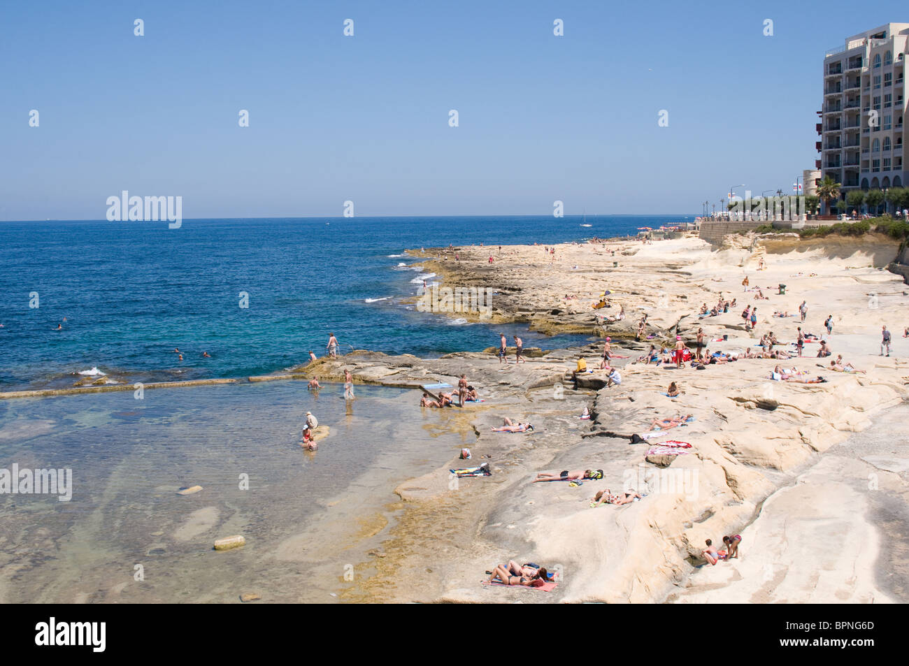 Sunbathers relax on the rocky beach in Sliema , Malta. On the left is a sea water pool that provides a safe area to splash about Stock Photo