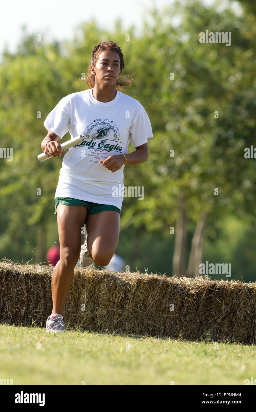 African-American female high school runners jumps hay bale on cross-country course during meet in Pflugerville, Texas Stock Photo