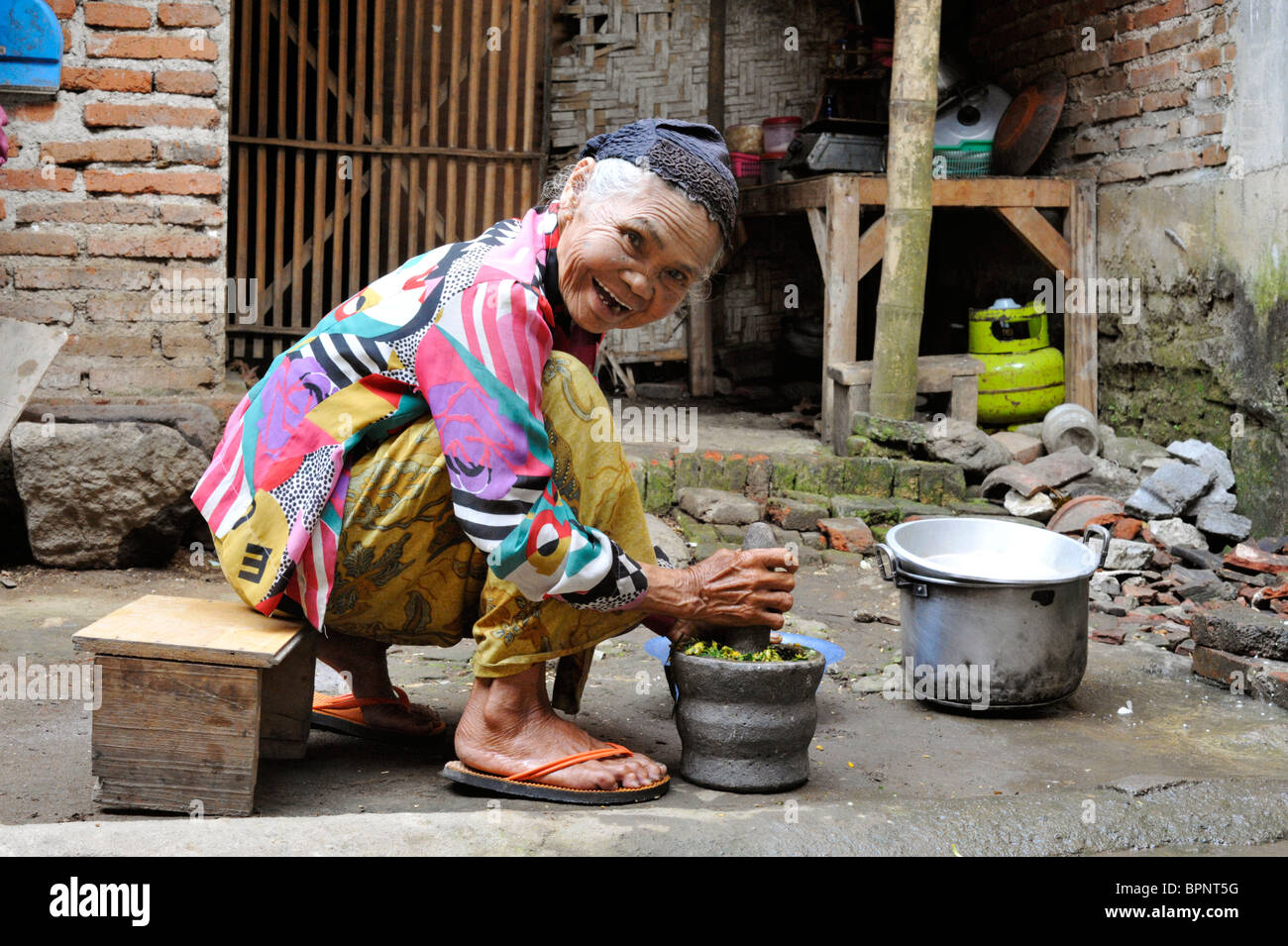 laughing elderly woman mixing traditional medicine in a mortar and pestle at her village home in java Stock Photo