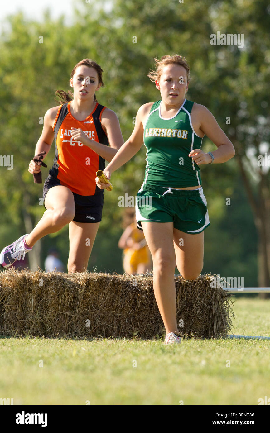 Anglo female high school runners jumps hay bale on crosscountry course