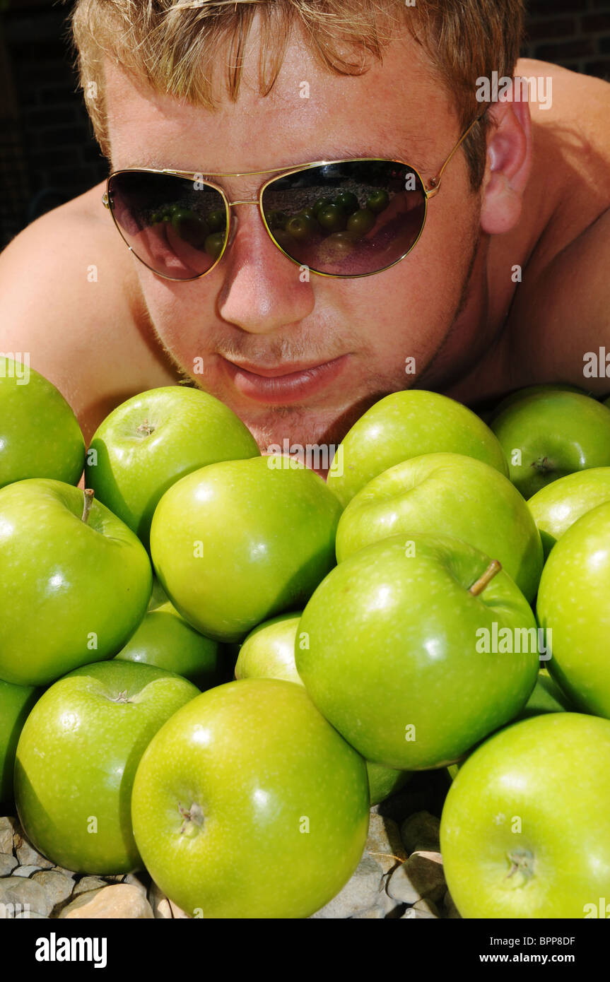 cool young white male laying in a pile of green apples Stock Photo