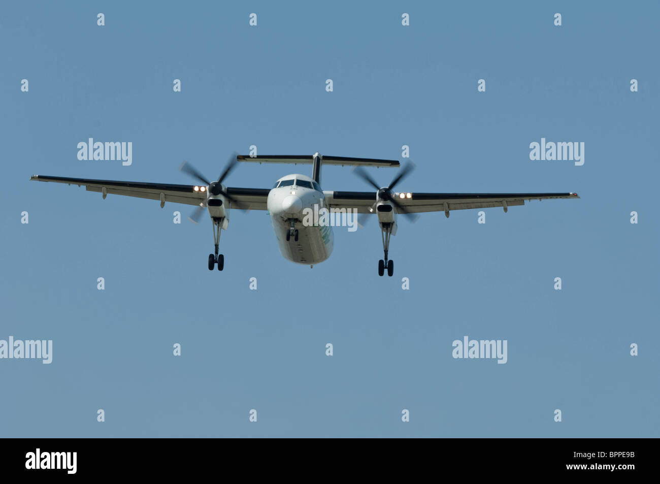 A Bombardier Dash-8 turboprop aircraft is on final approach to a runway with the landing down. Stock Photo