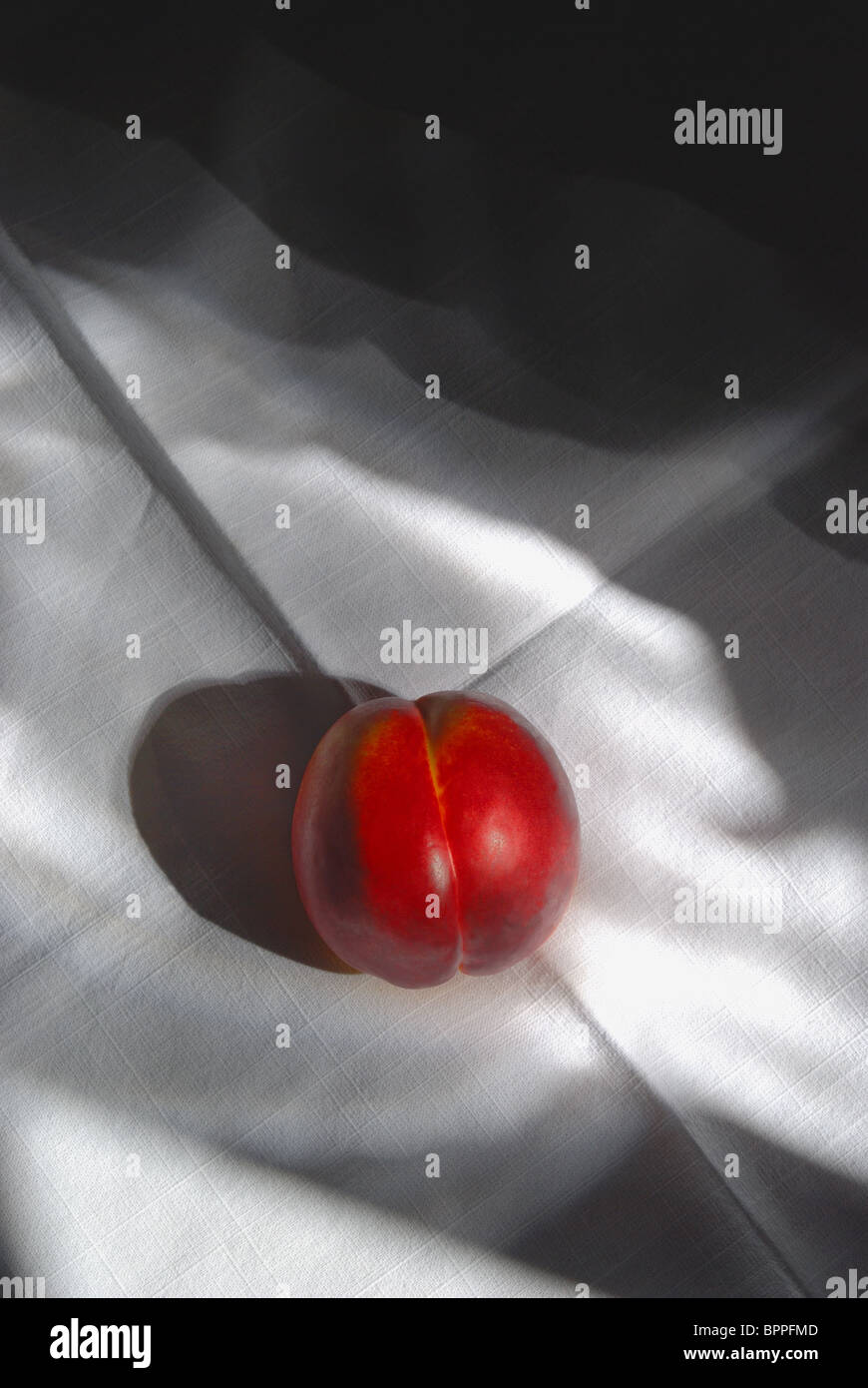 red peach, nectarine on a linen table cloth with atmospheric dappled shadows. still life. Stock Photo