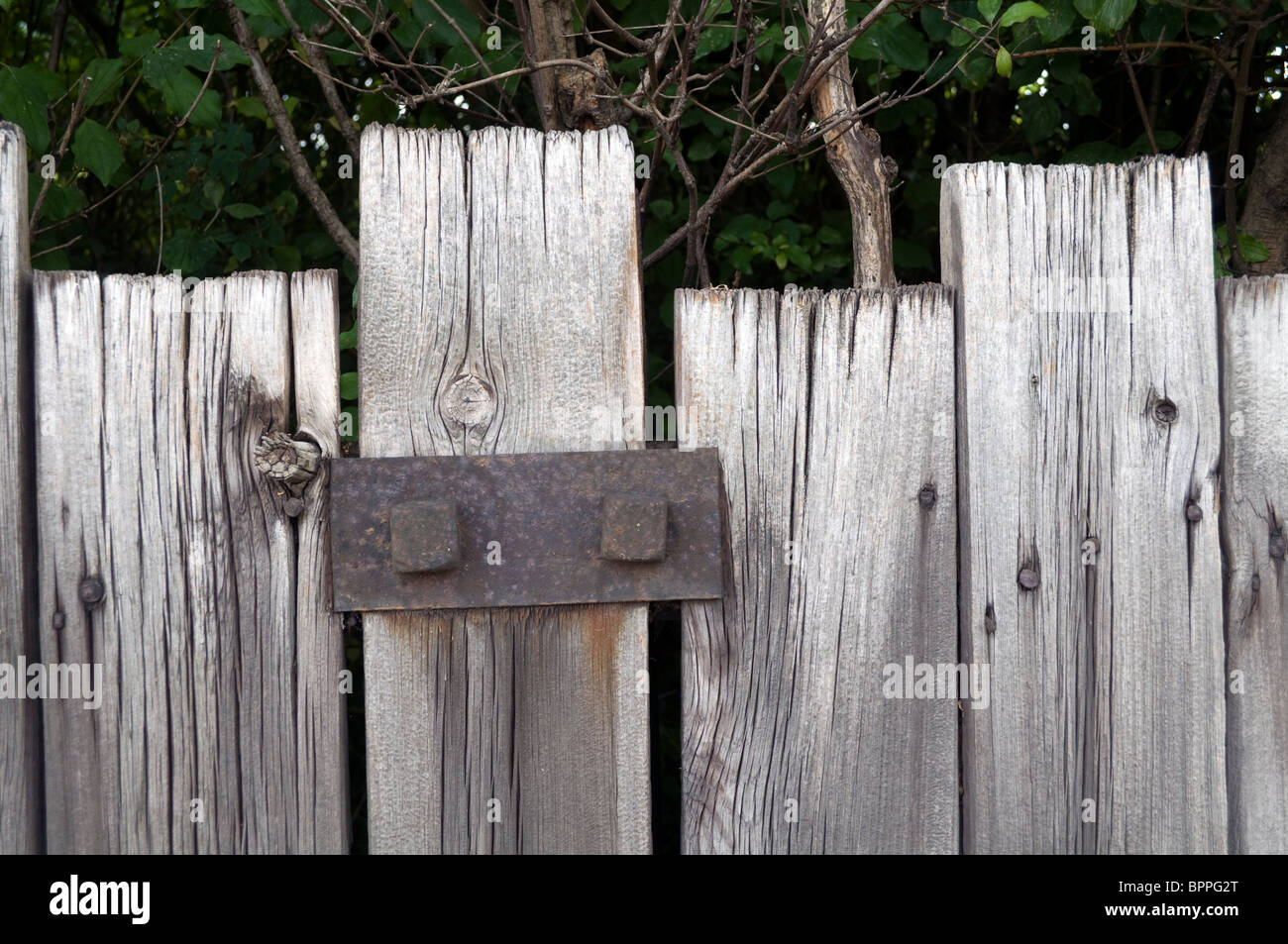 A rickety old wooden fence reinforced and repaired with a rusty metal bracket. Stock Photo