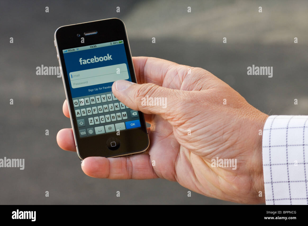 The iPhone 4 in the palm of a hand of a man, showing the Facebook app login. Stock Photo