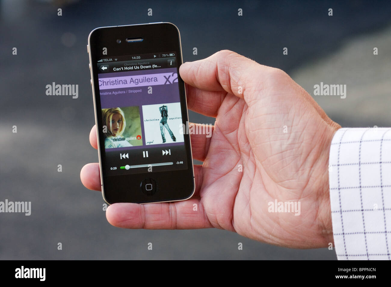 The iPhone 4 in the palm of a hand of a man, showing Spotify with Christina Aguilera. Stock Photo