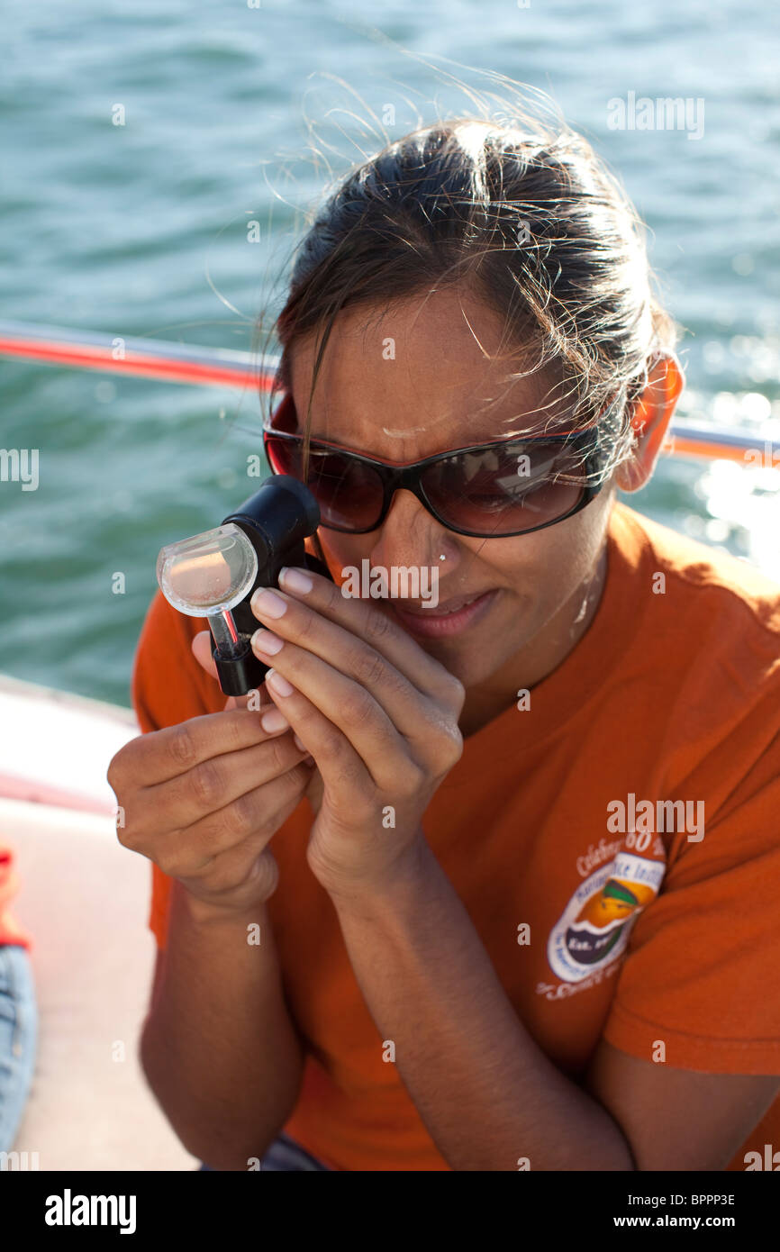 Female middle school teacher looks at a plankton specimen  on board research vessel during marine biology class field trip Stock Photo