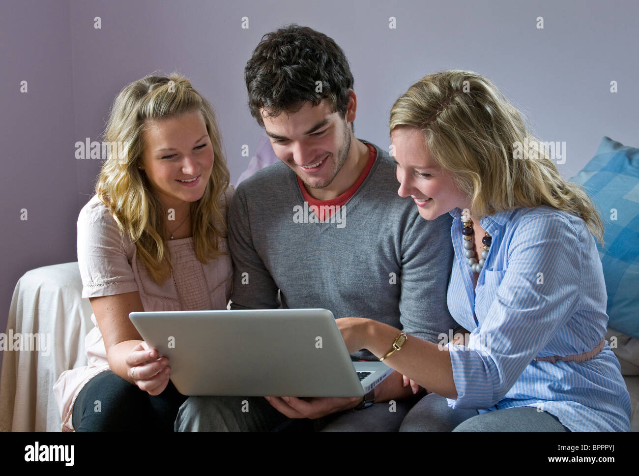 18-22 years flat mates Teenage boy and two girls relaxing indoors enjoy using their wireless home laptop computer Stock Photo