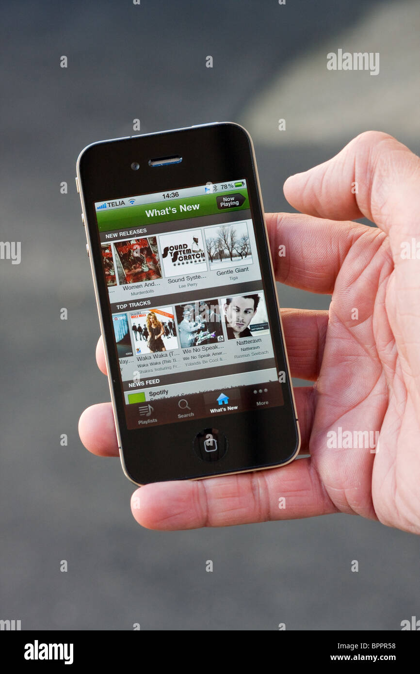 The iPhone 4 in the palm of the hand of a man. On the screen you can see the Spotify app. Stock Photo