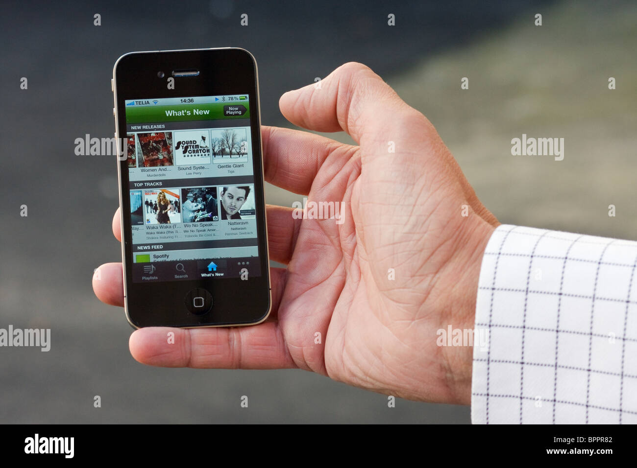 The iPhone 4 in the palm of the hand of a man. On the screen you can see the Spotify app. Stock Photo