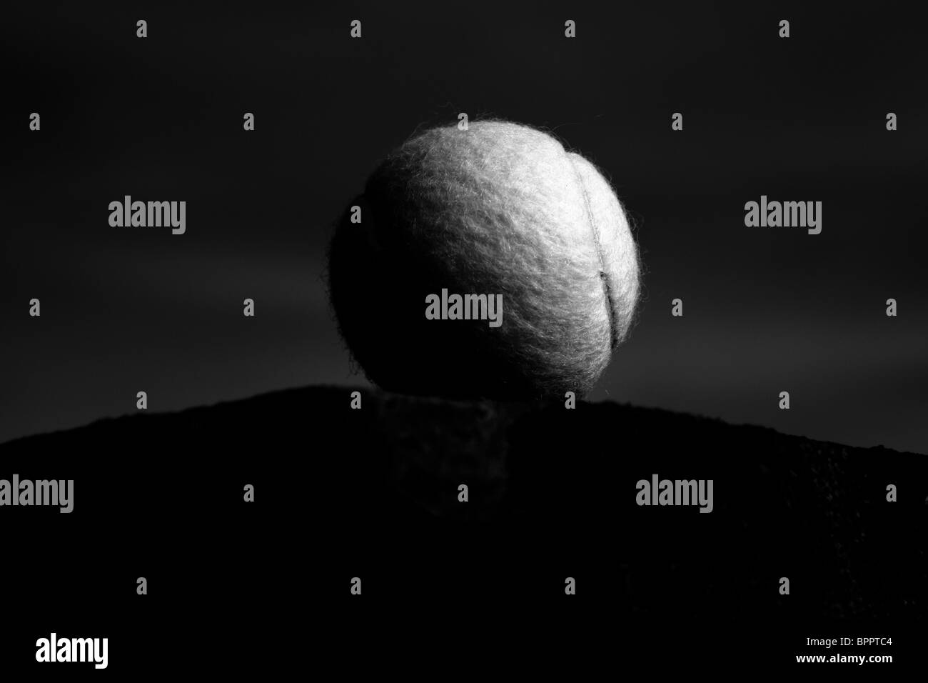 A solitary yet majestic tennis ball sits atop a platform lit from one side, as if by moonlight. Stock Photo