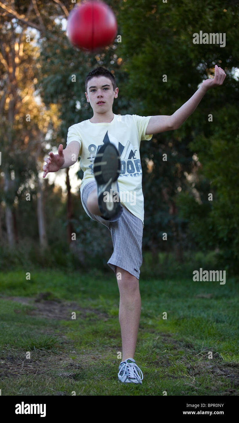 Teenage boy kicking AFL football Stock Photo