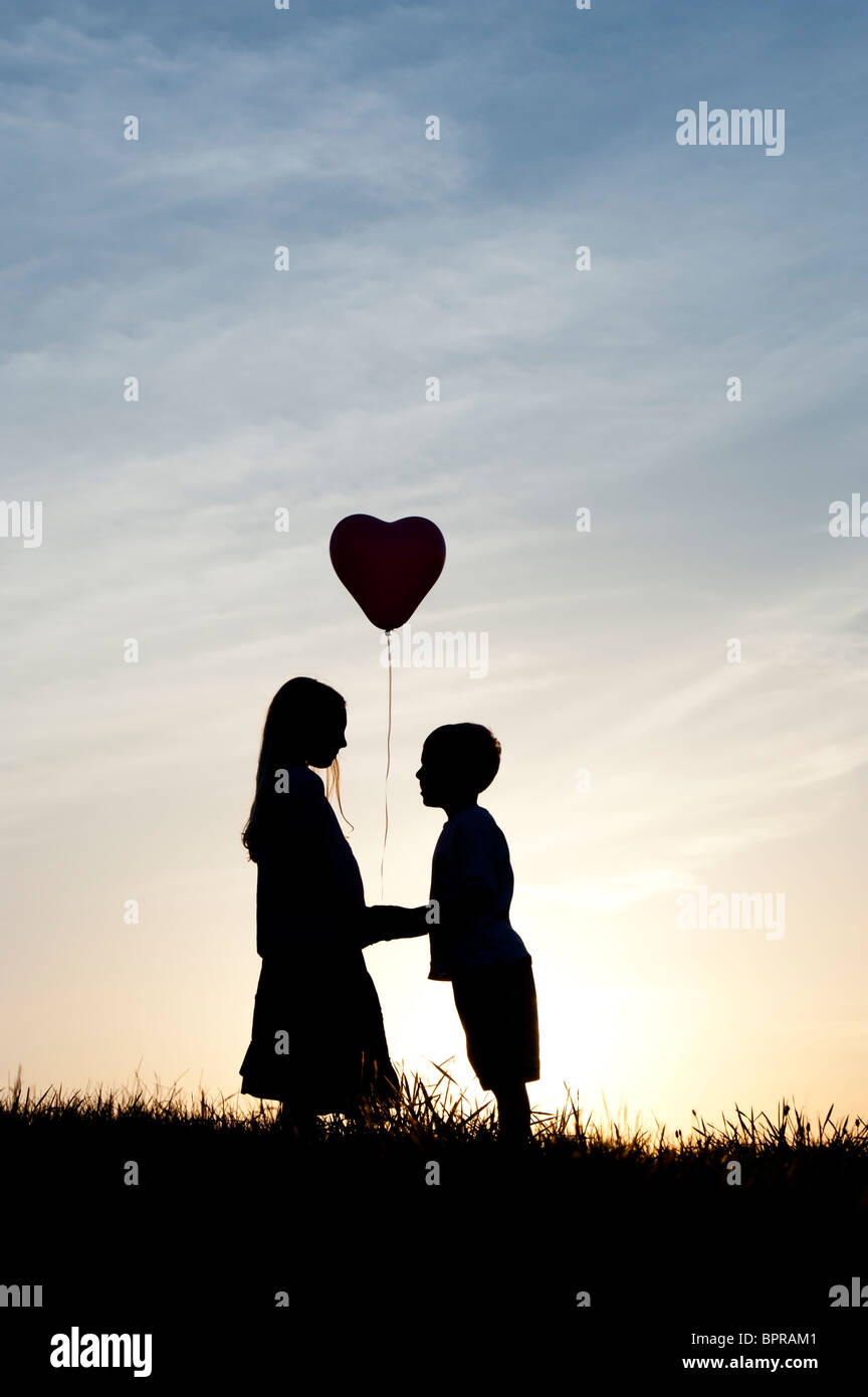 Silhouette Of A Young Girl And Boy Holding Hands With A Heart Shape Balloon At Sunset Stock Photo Alamy