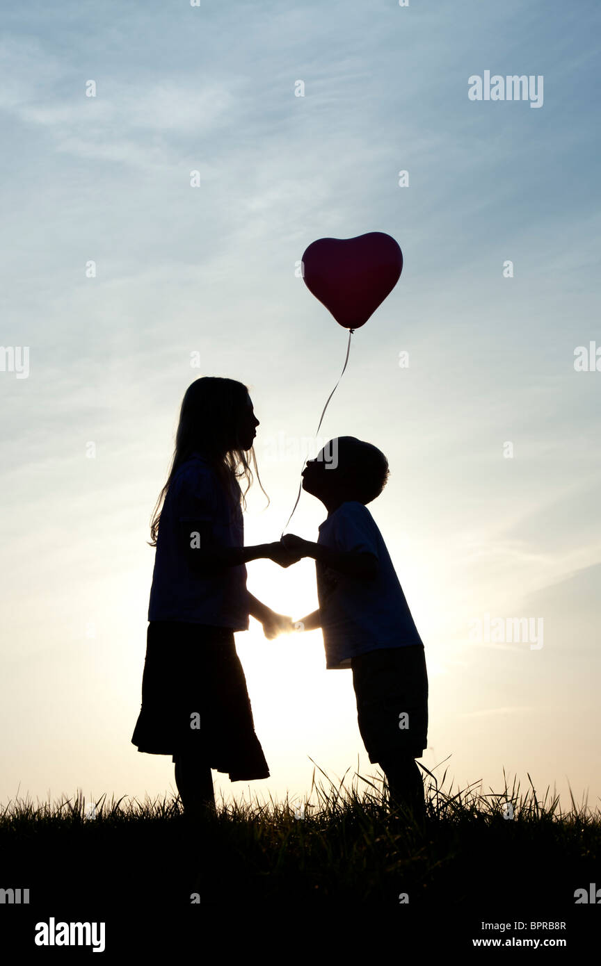 Silhouette Of A Young Girl And Boy Holding Hands And Kissing With A Heart Shape Balloon At Sunset Stock Photo Alamy