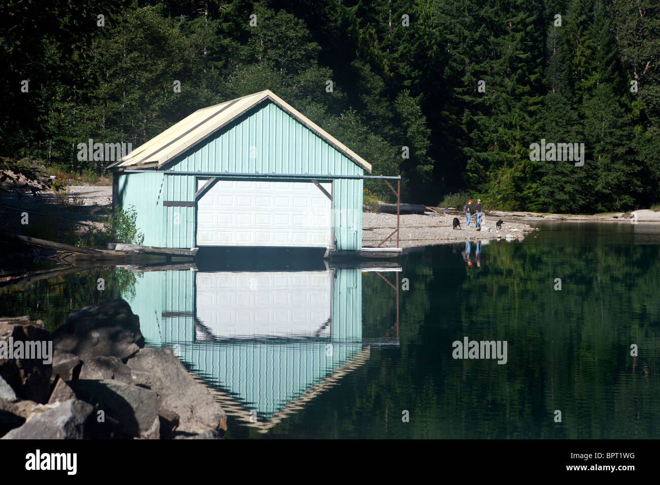 Boat house and reflection with two people walking dogs along the shore of Lake Diablo, North Cascades National Park, Washington Stock Photo