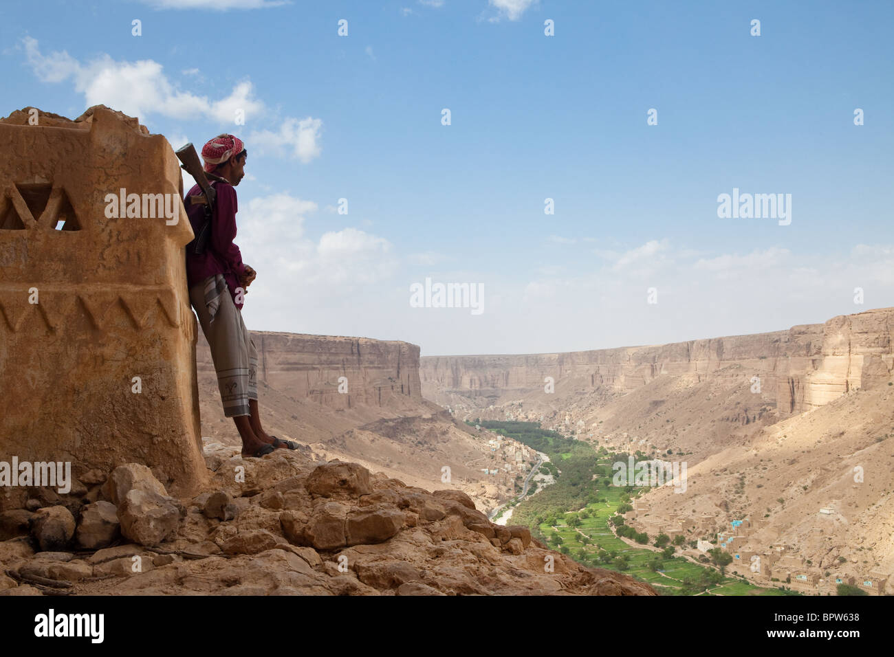 Yemeni man with AK-47 standing overlooking Wadi Do'an, Hadramaut, Yemen Stock Photo