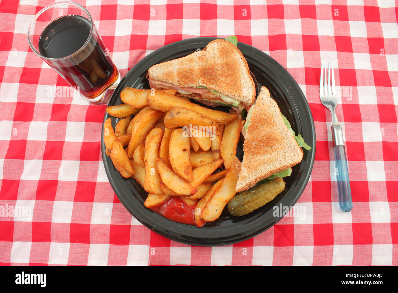 A plate of a bacon, lettuce and tomato sandwich also known as the BLT , french fried potato wedges, a pickle and catsup Stock Photo