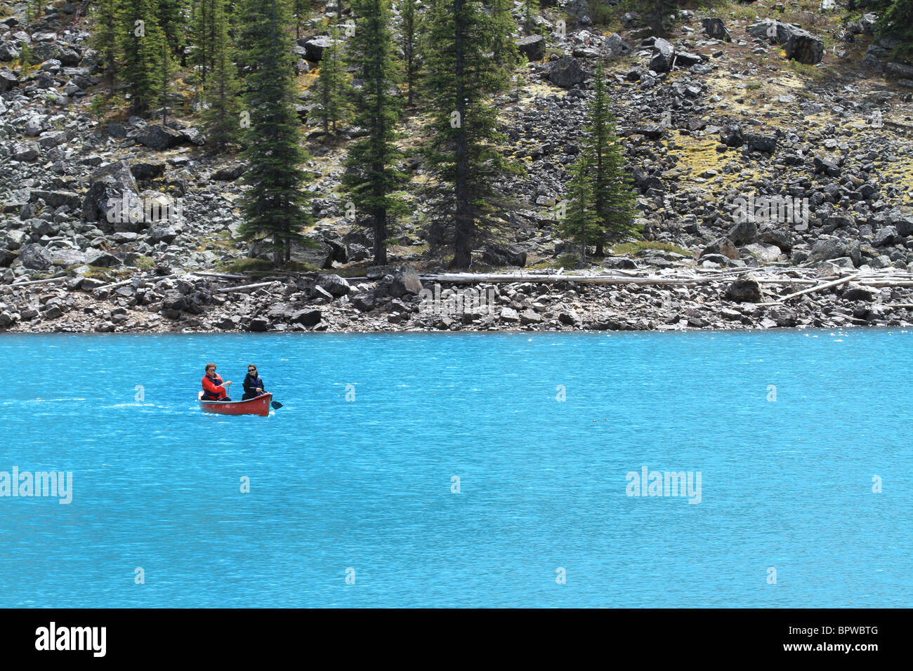 Couple paddles a bright red canoe across beautiful blue glacier lake in Banff National Park, Alberta, Canada. Stock Photo