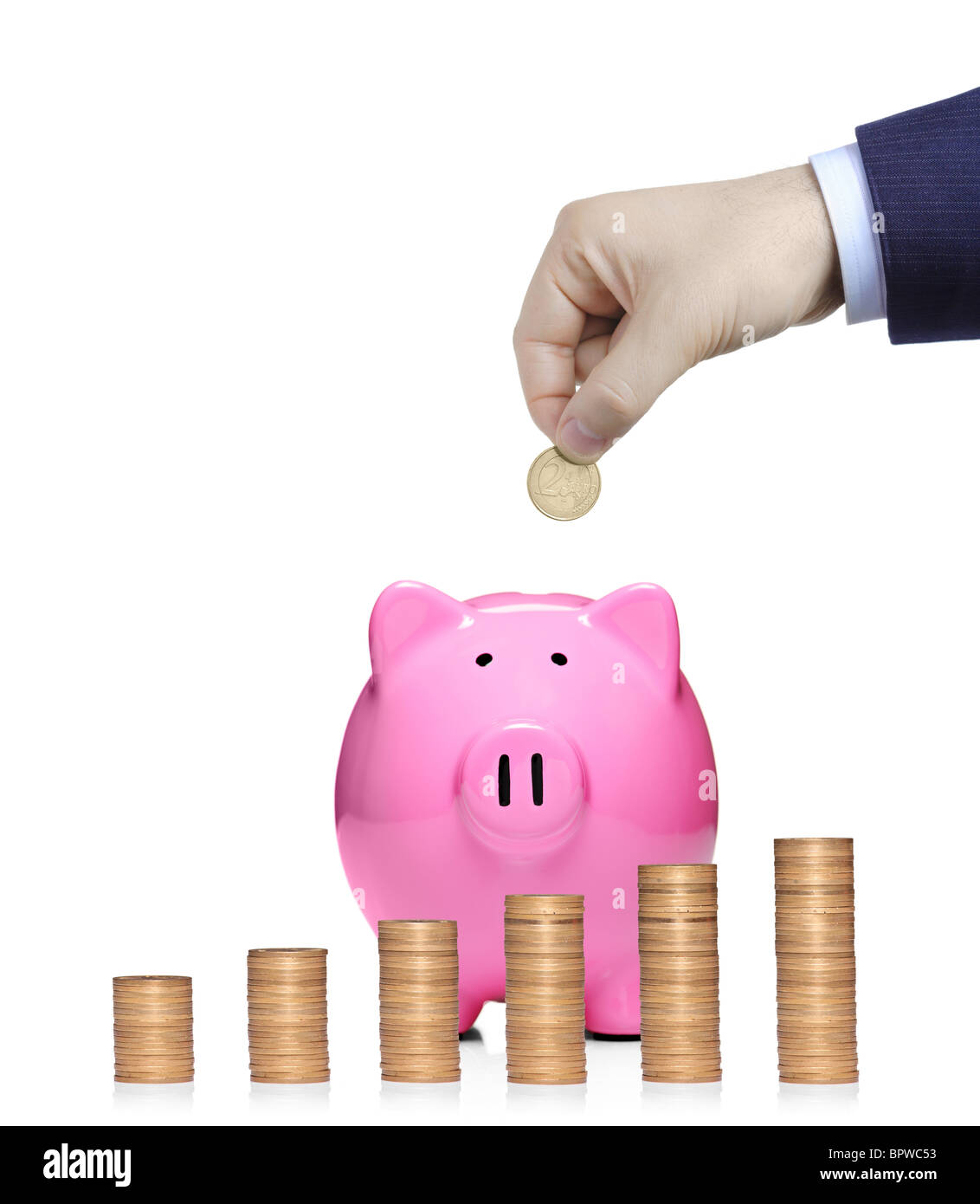 Person inserting a coin into a pink piggy bank with stack of coins in front showing growth Stock Photo