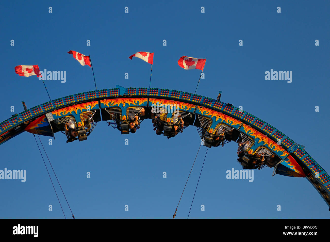 Riders hanging upside down on a roller coaster ride at the Canadian National Exhibition CNE funfair midway fairgrounds Toronto Canada flags Stock Photo