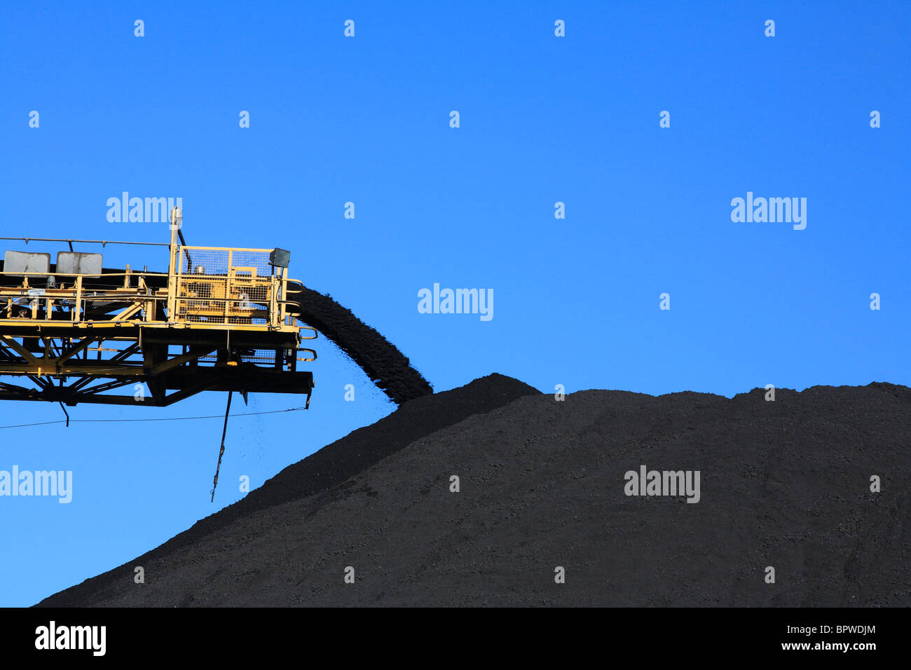 a large yellow conveyor belt carrying coal and emptying onto a huge pile. Kooragang Island, Newcastle, NSW, Australia Stock Photo