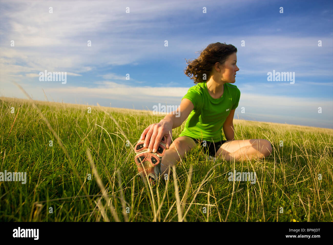 A female runner stretches and warms up on the grass before a long run Stock Photo