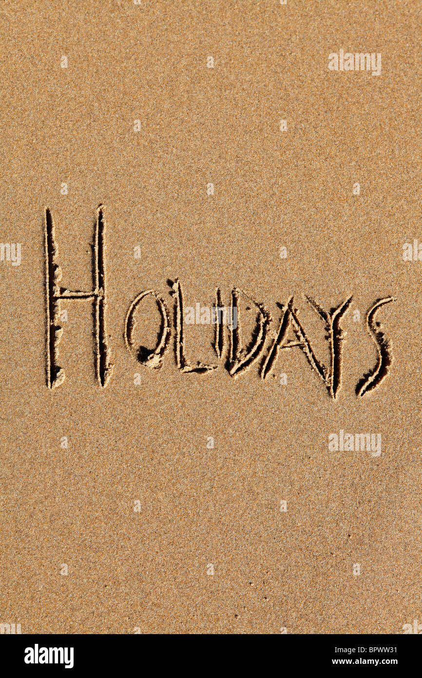The word "holidays" is written on the golden sands of a beach. Stock Photo