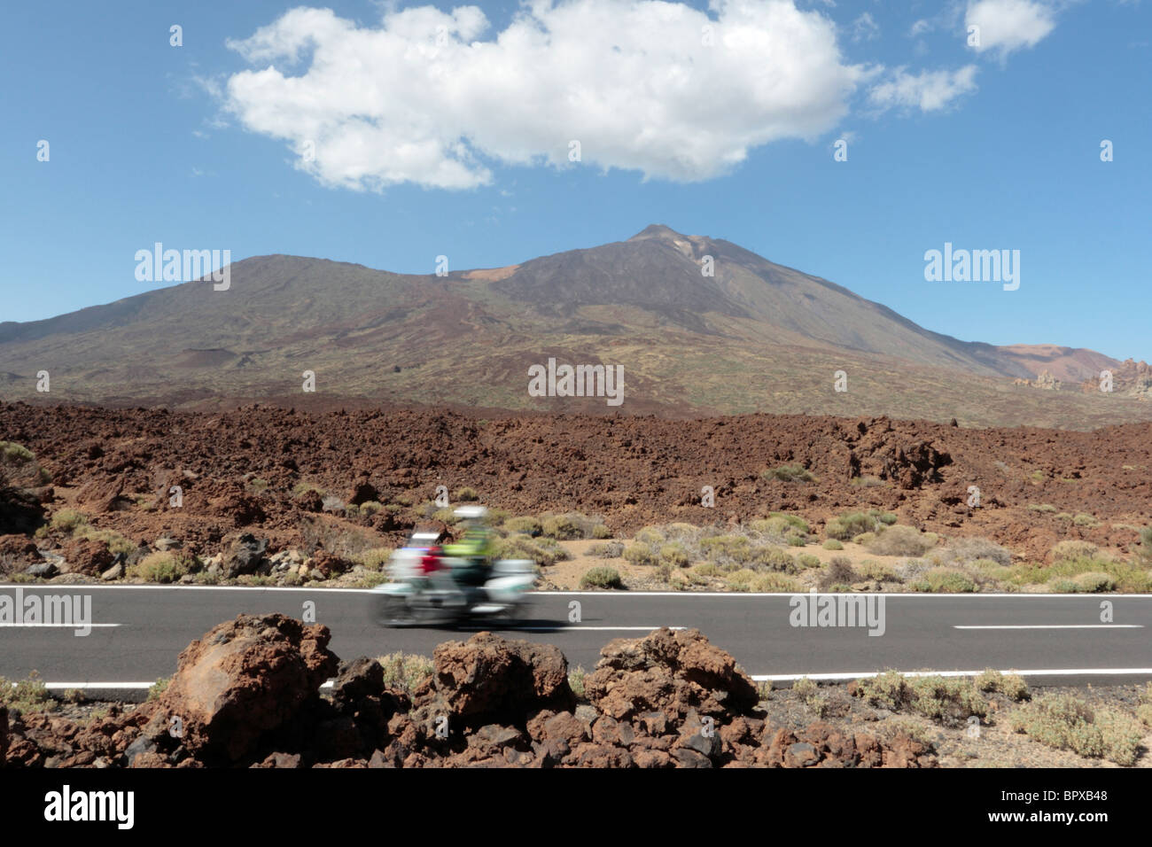 A Guardia Civil Trafico motorcyclist zooms past Teide in the Las Canadas del Teide National Park in Tenerife Canary Islands Stock Photo