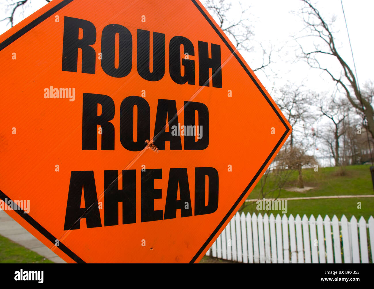 Orange warning sign reading rough road ahead Stock Photo
