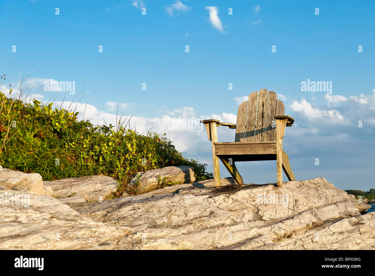 Adirondack chair sits on a rocky perch with a scenic coastal view