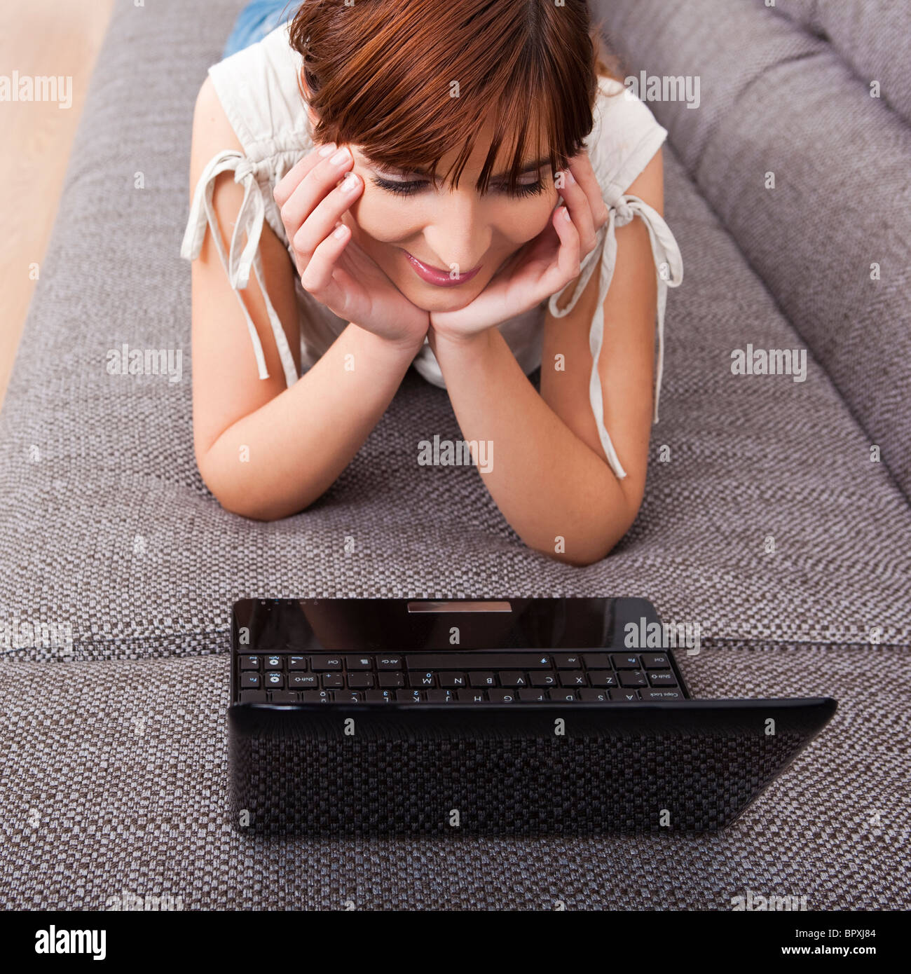 Beautiful woman at home lying on sofa and working with a laptop Stock Photo