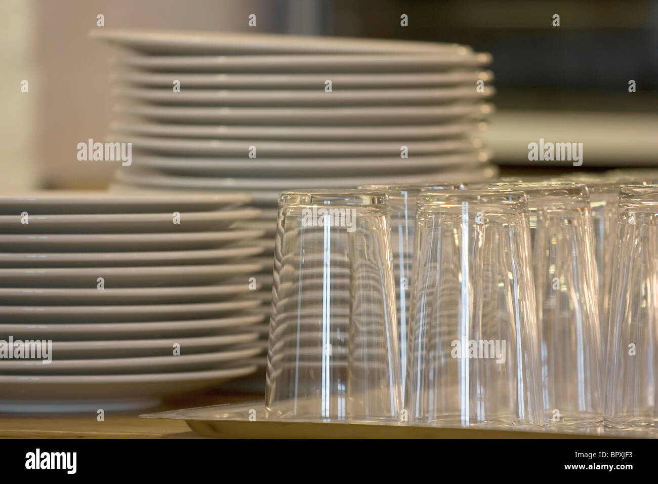 Upside down drinking glasses on a tray next to a stack of plates Stock